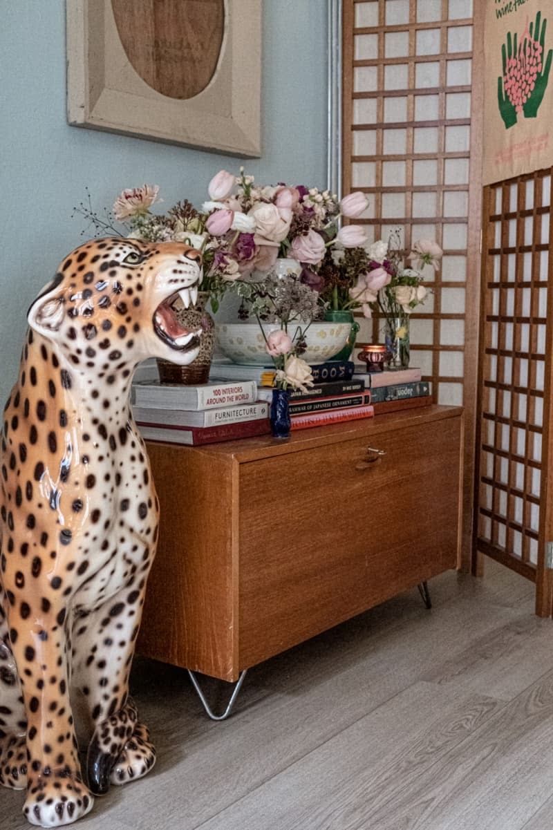 A leopard statue next to a wooden table stacked with hardcover books and flowers.