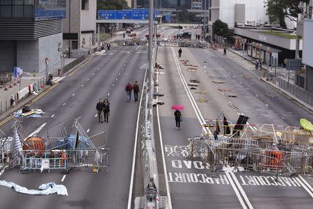 People walk past obstacles and barricades set up by pro-democracy protesters on a main road at the financial Central district in Hong Kong December 7, 2014. REUTERS/Bobby Yip