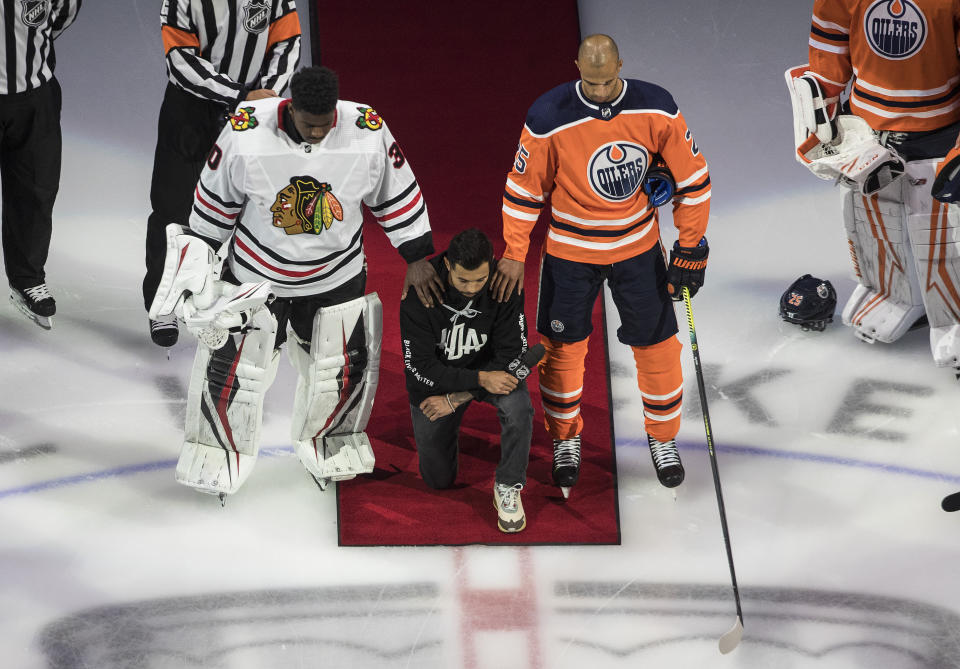 Minnesota Wild's Matt Dumba takes a knee during the national anthem flanked by Edmonton Oilers' Darnell Nurse, right, and Chicago Blackhawks' Malcolm Subban before an NHL hockey Stanley Cup playoff game in Edmonton, Alberta, Saturday, Aug. 1, 2020. (Jason Franson/The Canadian Press via AP)