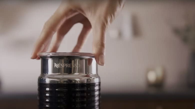 Close-up of a hand putting a lid on a Nespresso Aerocinno milk frother