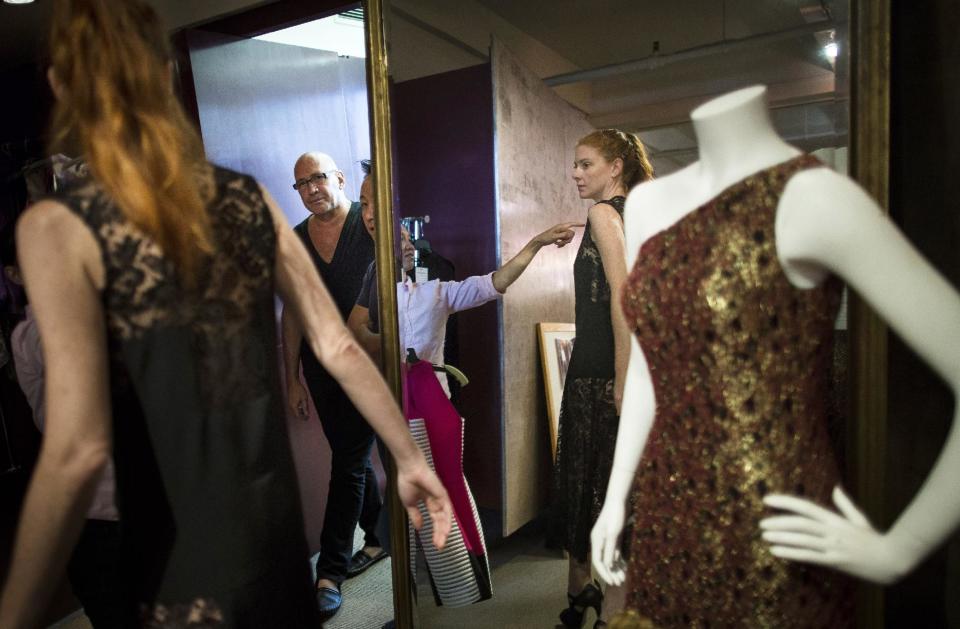 In this Aug 19, 2013 photo, fashion designer Carmen Marc Valvo, in glasses, watches his muse-model Taylor Foster be fitted for a dress at Valvo's New York studio. (AP Photo/John Minchillo)