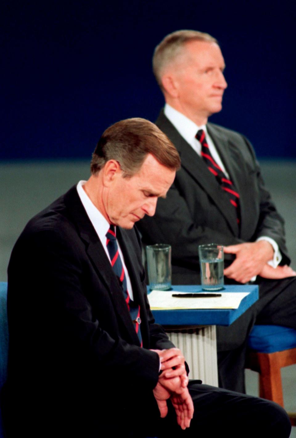 In this Oct. 15, 1992, file photo President George H.W. Bush looks at his watch during the 1992 presidential campaign debate with other candidates, Independent Ross Perot, top, and Democrat Bill Clinton, not shown, at the University of Richmond, Va.