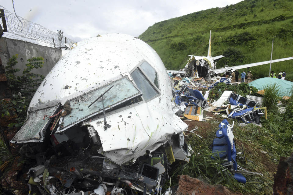 People stand by the debris of the Air India Express flight that skidded off a runway while landing in Kozhikode, Kerala state, India, Saturday, Aug. 8, 2020. The special evacuation flight bringing people home to India who had been trapped abroad because of the coronavirus skidded off the runway and split in two while landing in heavy rain killing more than a dozen people and injuring dozens more. (AP Photo/Shijith Sreedhar)