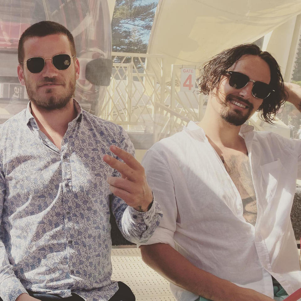 Jesse Burford wearing a white shirt and black sunglasses sitting next to another man in a shirt and sunglasses