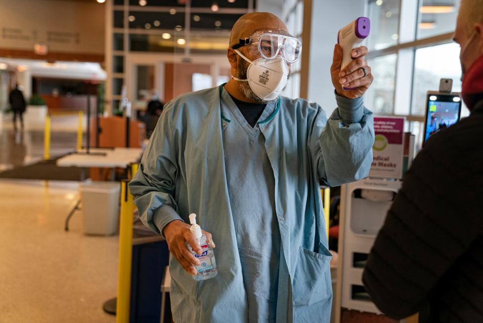 Hospital entrance screener and patient support technician Octave LeDuff, of Pontiac, takes a visitor's temperature at St. Joseph Mercy Oakland Hospital in Pontiac on Monday, Jan. 24, 2022, during an omicron surge.