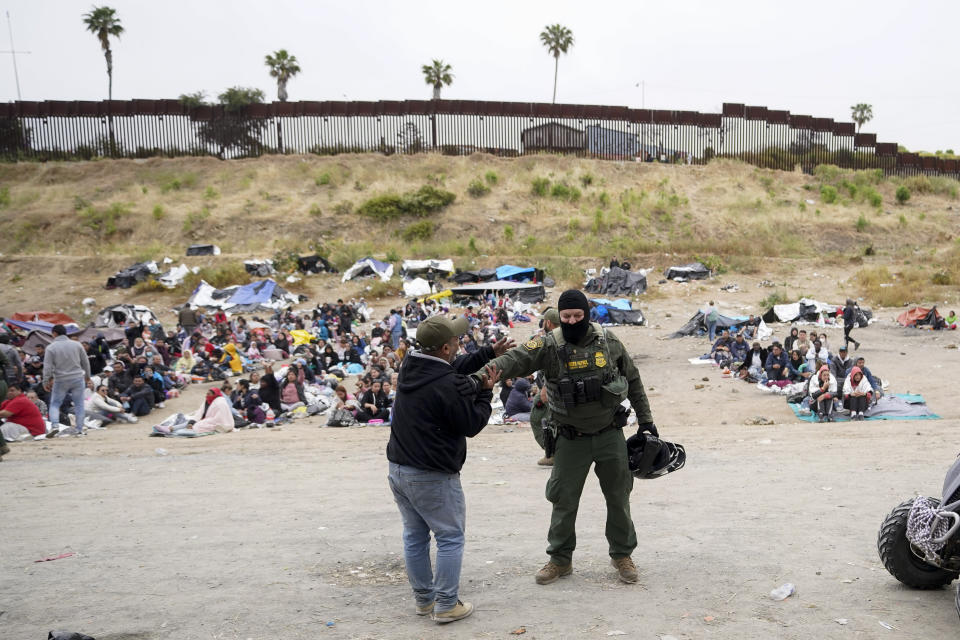 Un hombre bromea con un agente de la Patrulla Fronteriza de Estados Unidos mientras él y otros migrantes aguardan entre dos muros fronterizos para solicitar asilo, el viernes 12 de mayo de 2023, en San Diego. Cientos de migrantes siguen aguardando entre los dos muros, muchos de ellos durante días. A partir del viernes, Estados Unidos modificó sustancialmente la forma en que recibe a migrantes, al poner fin a una restricción al asilo que estuvo vigente durante tres años e implementar una serie de nuevas normas estrictas que el gobierno del presidente Joe Biden espera estabilizarán la frontera entre Estados Unidos y México y obligarán a los migrantes a solicitar el ingreso desde su país, evitando así que hagan el peligroso recorrido hacia el norte. (AP Foto/Gregory Bull)