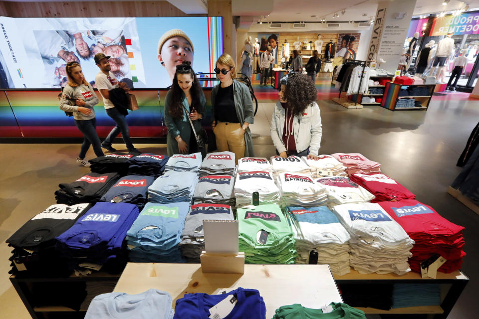 In this June 14, 2019, photo a pair of shoppers, center, in the Levi's store in New York's Times Square, survey a T-shirt display. Levi Strauss & Co.’s new flagship in Manhattan’s Time Square features larger dressing rooms with call buttons and tailors who can add trims and patches to customers’ jeans. (AP Photo/Richard Drew)
