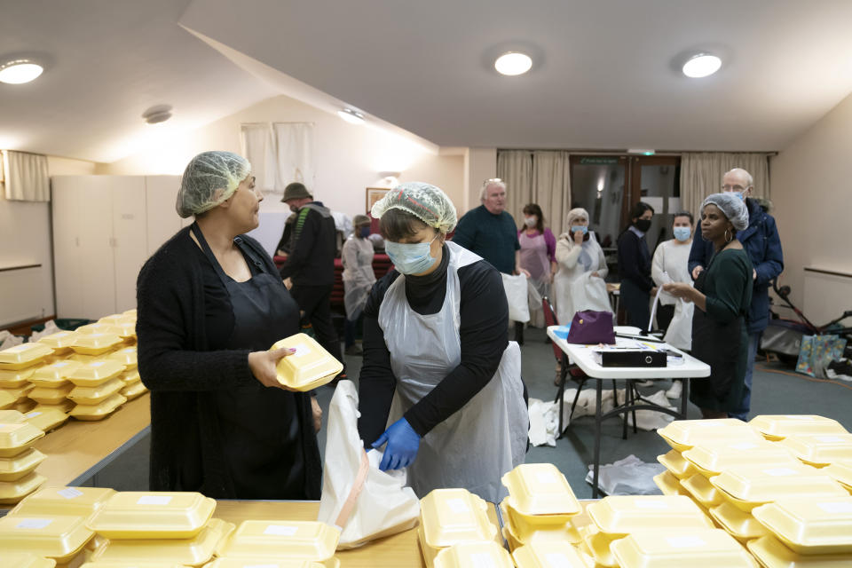 Chief coordinator Glenda Andrew, right, talks to volunteer Diane Proctor, foreground left, as members of the Preston Windrush Covid Response team dish out West Indian meals, at the Xaverian Sanctuary, in Preston, England, Friday Feb. 19, 2021. Once a week they distribute meals to people in Preston and surrounding communities in northwestern England that have recorded some of the U.K.’s highest coronavirus infection rates. The meal program grew out of Andrew’s work with Preston Windrush Generation & Descendants, a group organized to fight for the rights of early immigrants from the Caribbean and other former British colonies who found themselves threatened with deportation in recent years. (AP Photo/Jon Super)