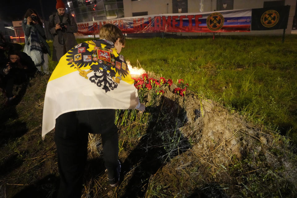 A man places flowers at an informal memorial next to the former 'PMC Wagner Centre' in St. Petersburg, Russia, Thursday, Aug. 24, 2023, with a banner that reads, 'PMC Wagner, we are together,' in the background. Russia's civil aviation agency says mercenary leader Yevgeny Prigozhin was on board a plane that crashed north of Moscow. (AP Photo/Dmitri Lovetsky)