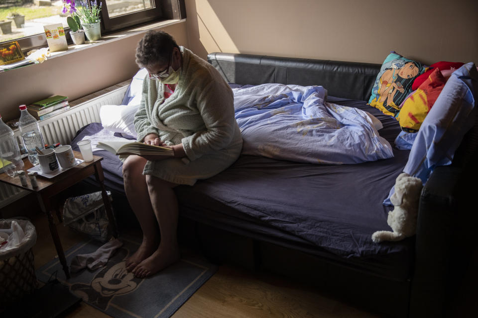 In this photo taken on Wednesday, April 29, 2020, Diane Wanten, 61, reads a book as she recuperates in quarantine at her son's house in Alken, Belgium. Wanten was recently released into home quarantine from the hospital after being treated for two weeks at the Jessa Hospital ICU ward for COVID-19 coronavirus patients. (AP Photo/Francisco Seco)