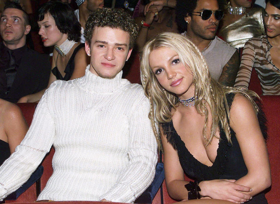 Justin in a knit turtleneck sitting with Britney Spears, in a low-cut outfit