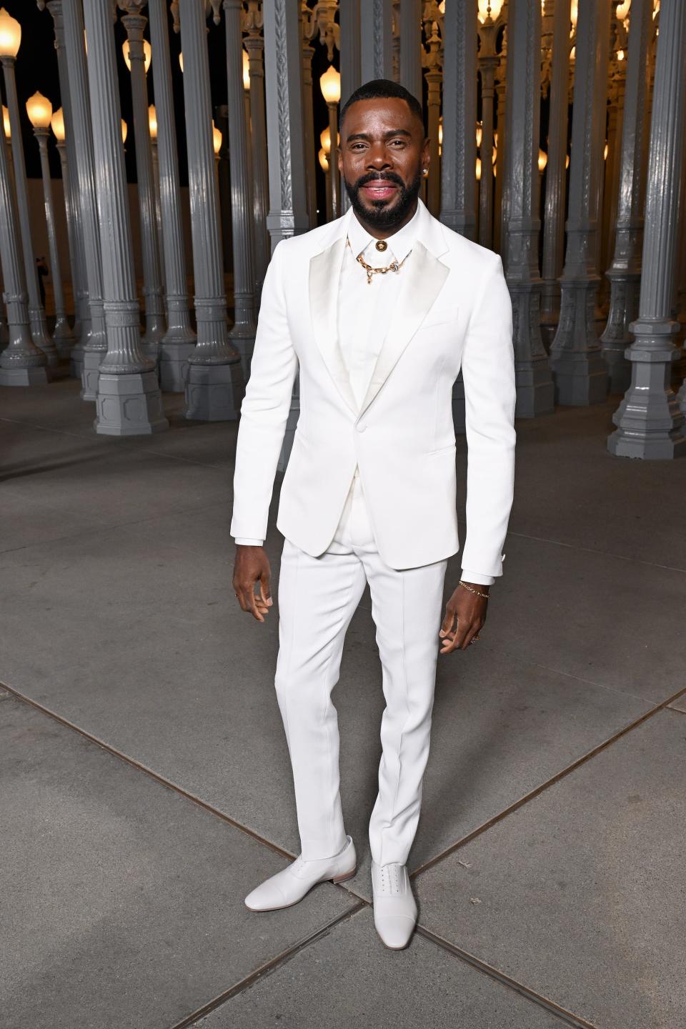 Colman Domingo stands in an all white outfit in front of pillars.