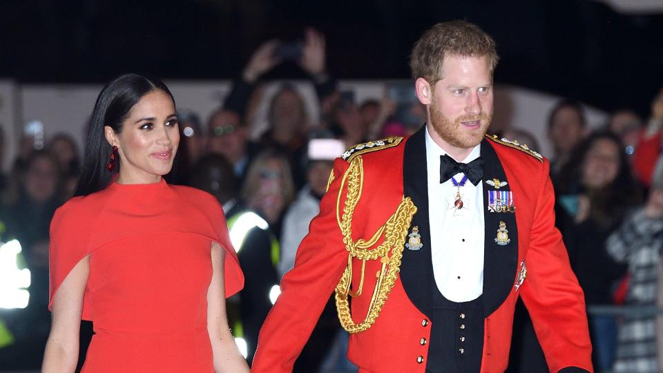 Prince Harry in red jacket and Meghan in red caped dress