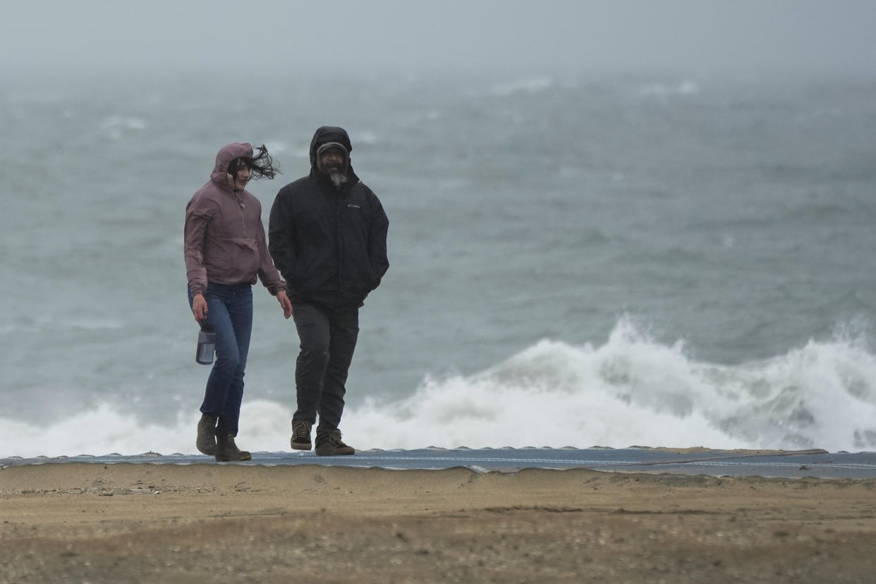 People walk along the beach on Friday, Feb. 24, 2023, in Huntington Beach, Calif. California and other parts of the West faced heavy snow and rain Friday from the latest winter storm to pound the U.S. (AP Photo/Ashley Landis)
