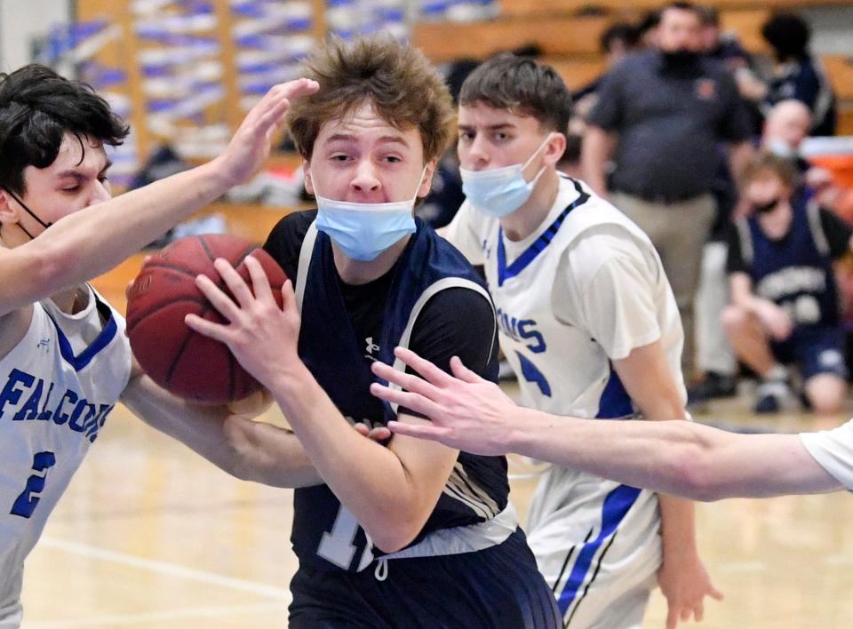 In this Feb. 17, 2022 photo, Finn Hyora of Monomoy drives the lane between Brady Johnston (left) and Sean Fancer of Mashpee.