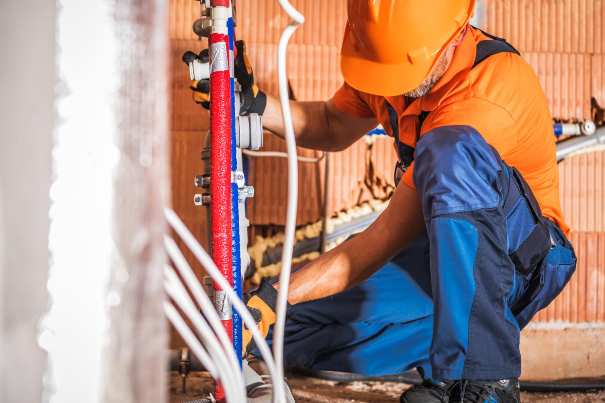 Caucasian Plumber Wearing Orange Hard Hat Installing Bathroom Water Supply Inside Newly Developed Concrete Blocks Building. Construction Site Theme.