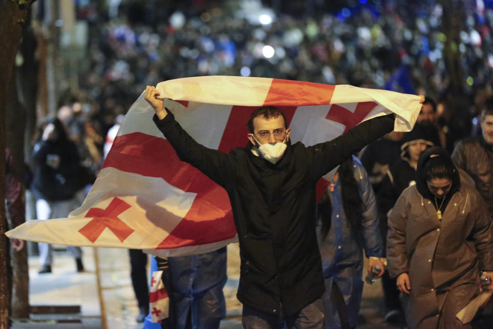 A demonstrator holds a Georgian national flag as he walks in front of the Parliament building during an opposition protest against "the Russian law" in the center of Tbilisi, Georgia, on Sunday, May 12, 2024. Daily protests are continuing against a proposed bill that critics say would stifle media freedom and obstruct the country's bid to join the European Union. (AP Photo/Zurab Tsertsvadze)