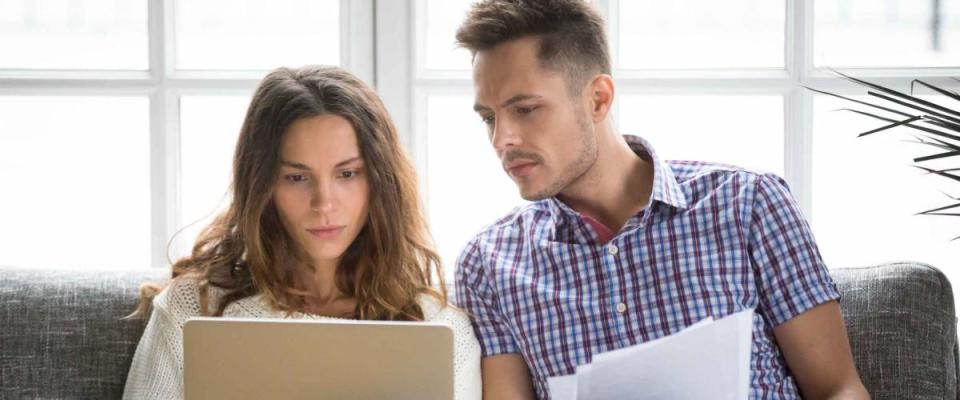 Couple sitting on a couch looking at papers and laptop, looking concerned