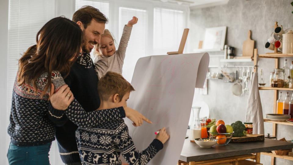 copy space shot of parents bonding and having fun with their teenage son and their toddler daughter they are standing in their living room and drawing on a piece of paper that is hanging on easel