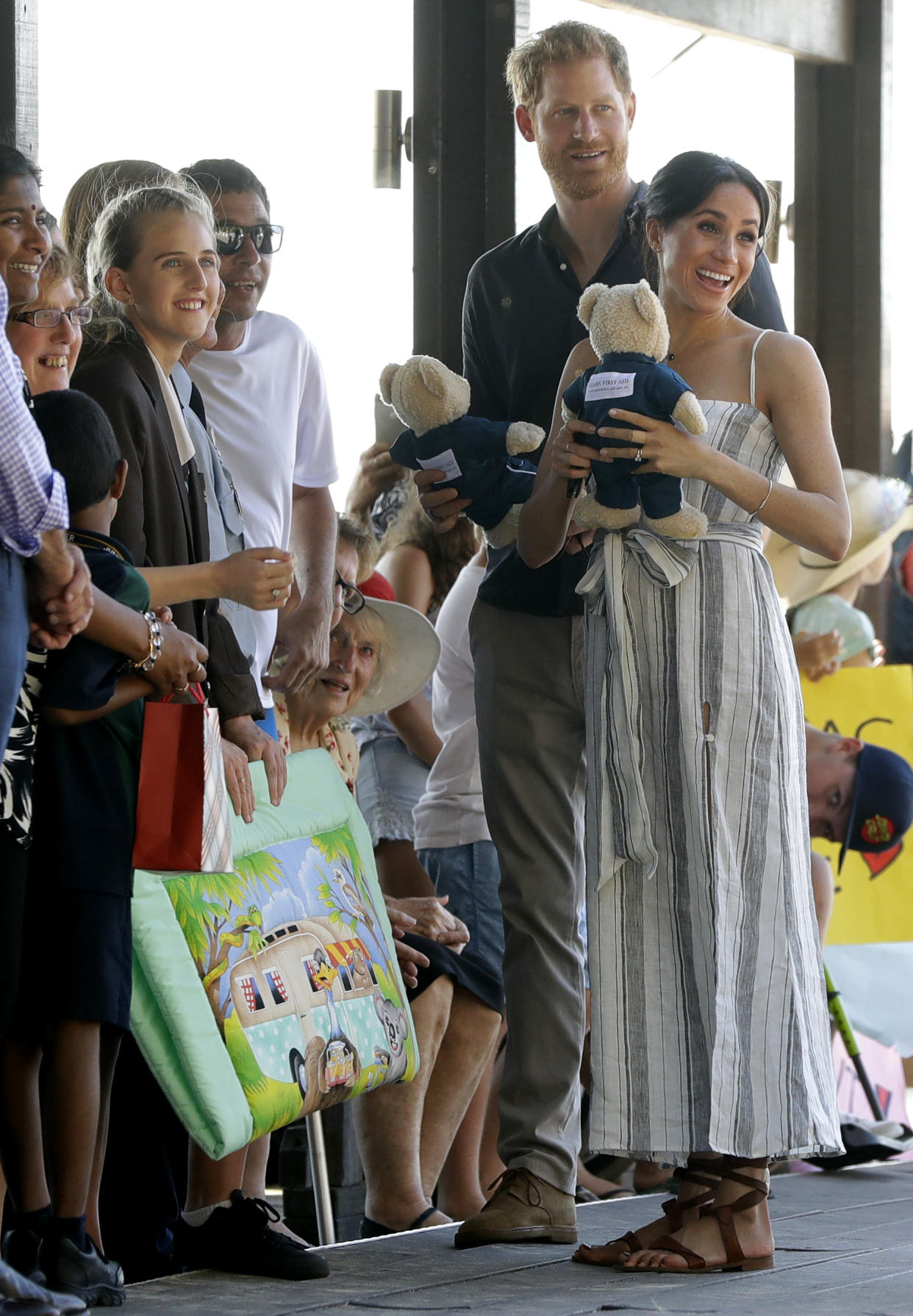 Britain's Prince Harry, second from right, and Meghan, Duchess of Sussex receive gifts from the crowd as they walk along Kingfisher Bay Jetty during a visit to Fraser Island, Australia, Monday, Oct. 22, 2018. Prince Harry and his wife Meghan are on day seven of their 16-day tour of Australia and the South Pacific. (AP Photo/Kirsty Wigglesworth, Pool)