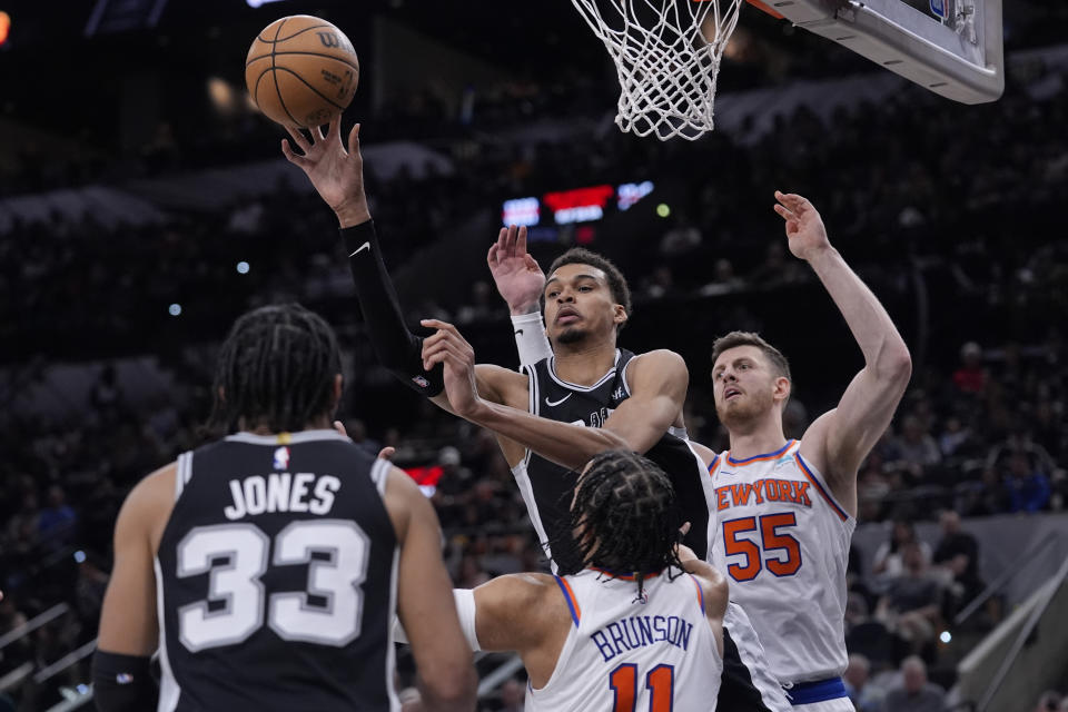 San Antonio Spurs center Victor Wembanyama, center, passes the ball over New York Knicks guard Jalen Brunson (11) during the second half of an NBA basketball game in San Antonio, Friday, March 29, 2024. (AP Photo/Eric Gay)