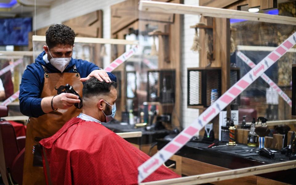 A hairdresser cuts the hair of a client sitting in a space separated by transparent panes at a hair salon which reopened on Monday after being closed for more than two months due to the pandemic. - INA FASSBENDER/AFP via Getty Images