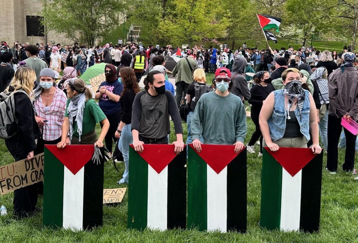 Masked protesters at IU's Dunn Meadow on Friday, April 26, 2024, display Palestinian flags made of wood. Tents can be seen in the background.