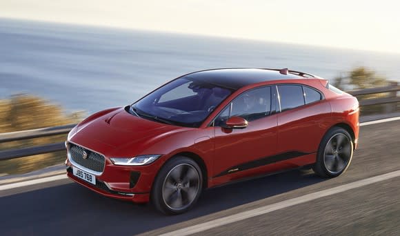 A red Jaguar I-Pace, a sleek electric crossover SUV, on an ocean road.