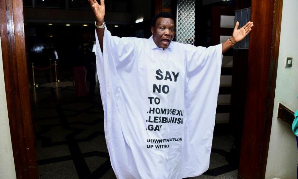 An Ugandan member of parliament, John Musira, in a white gown that has anti-LGBTQ+ slogans emblazoned on it.