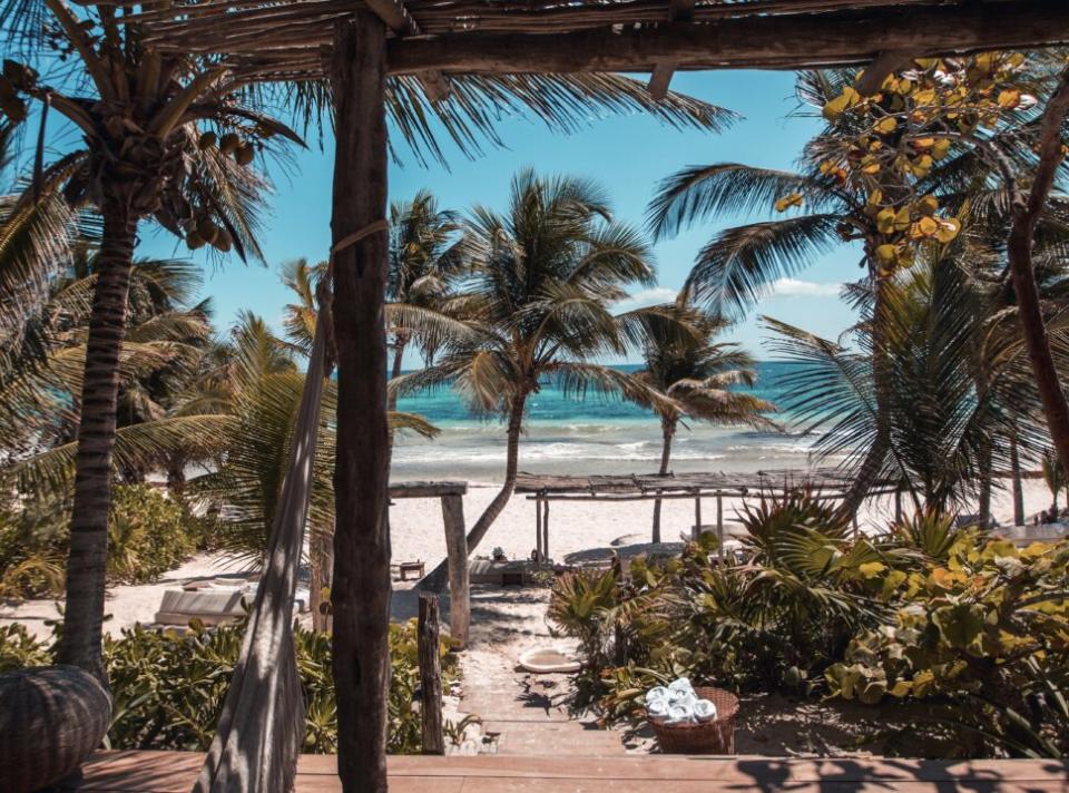 tulum vs cancun Pictured: a beach side resort with surrounding palm trees in Tulum