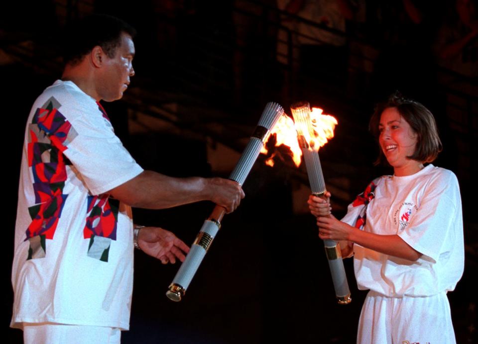 American swimmer Janet Evans passes the Olympic flame to Muhammad Ali during the 1996 Summer Olympic Games Opening Ceremony in Atlanta Friday, July 19, 1996. (AP Photo/Michael Probst)