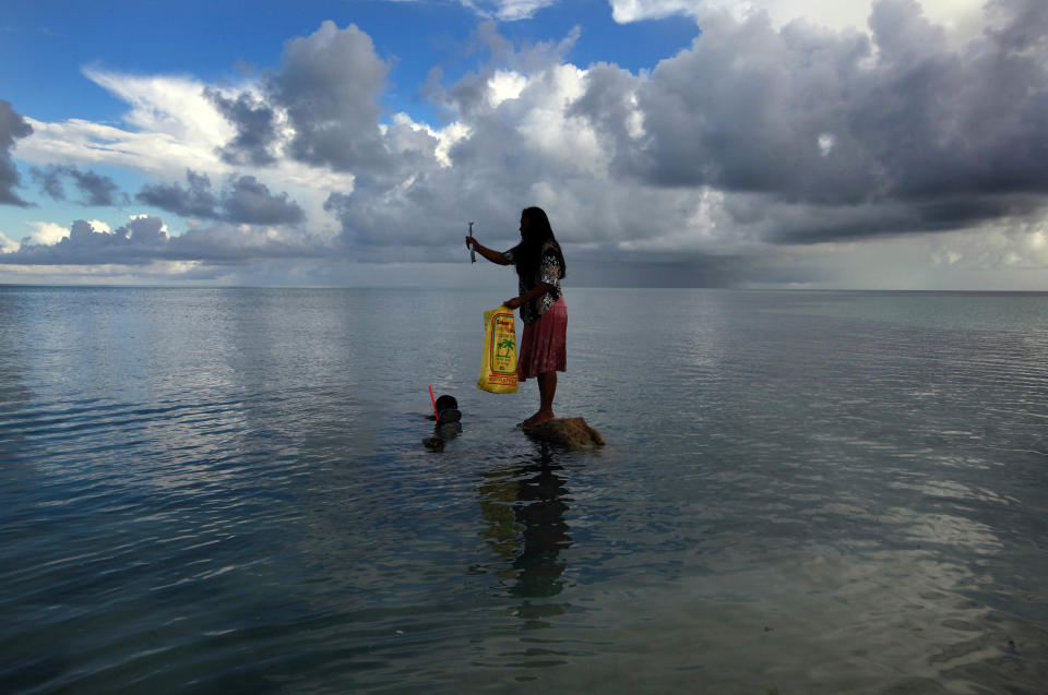 A woman stands on top of a rock holding a fish her husband just caught off Bikeman islet, located off South Tarawa in the central Pacific island nation of Kiribati.