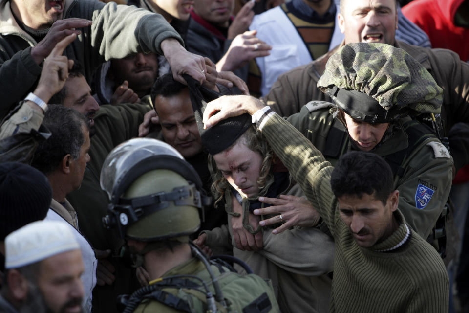 Palestinians hit an Israeli settler, center, who was briefly detained by Palestinian villagers as Israeli soldiers evacuate him near the West Bank village of Qusra, Jan. 7, 2014. (AP Photo/Nasser Ishtayeh)