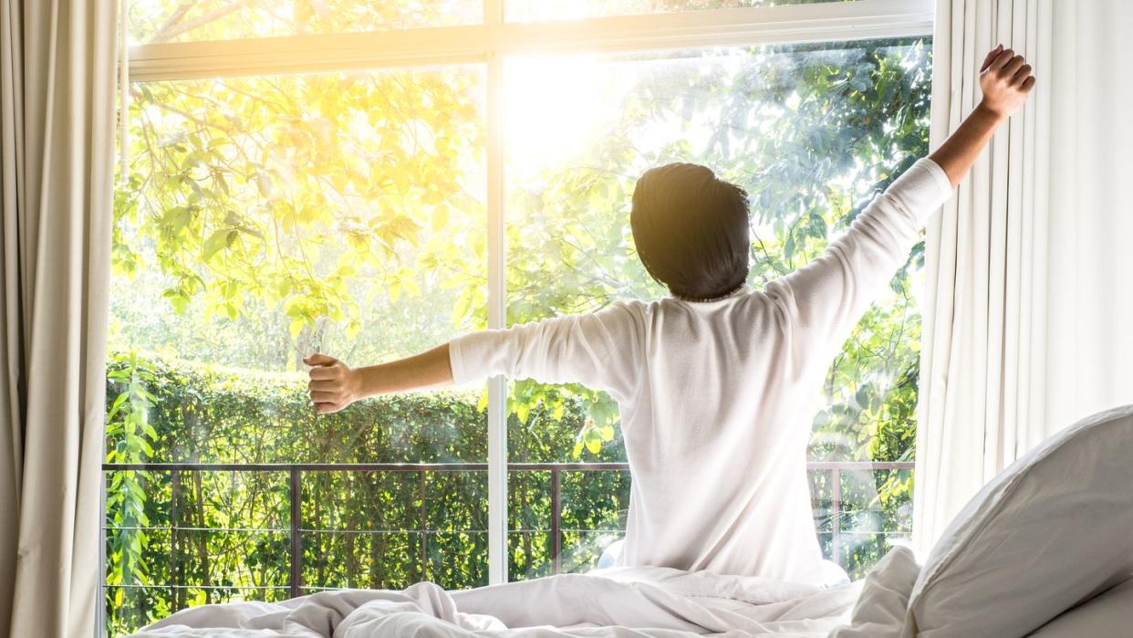 daylight saving sleep - Rear View Of Man Stretching Arms While Sitting On Bed At Home