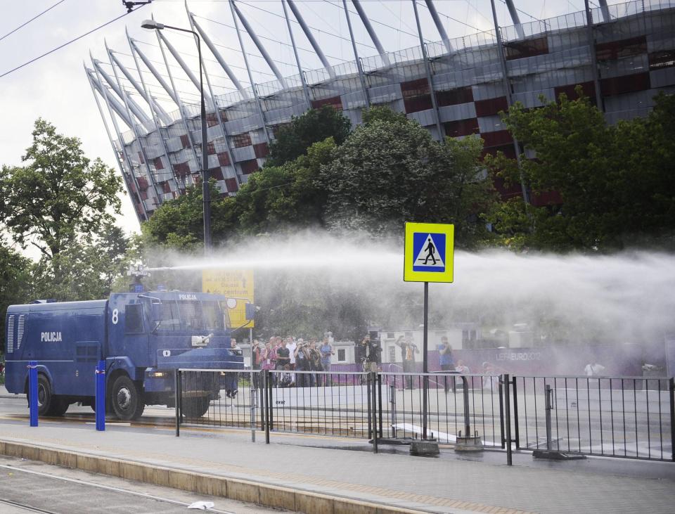 Polish police deploy water cannons to break up the fighting as football fans look on in the distance.