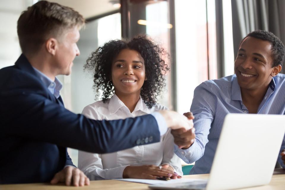 A bank employee shaking hands with prospective clients while seated in an office.