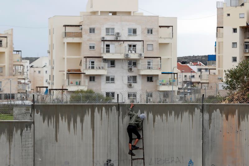 Palestinian demonstrator uses a ladder to climb a section of the Israeli barrier as the Jewish settlement of Modiin is seen in the background during a protest against Trump's Middle East peace plan, in the village of Bilin in the Israeli-occupied West Bank