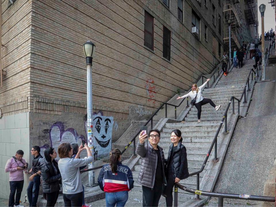 People pose on the steps between two apartment buildings, Monday Oct. 28, 2019, in the Bronx borough of New York. The stairs have become a tourist attraction in recent weeks since the release of the movie “Joker.” In the movie, lead actor Joaquin Phoenix dances as he goes down the steps, wearing a bright red suit and clown makeup. (AP Photo/Bebeto Matthews)