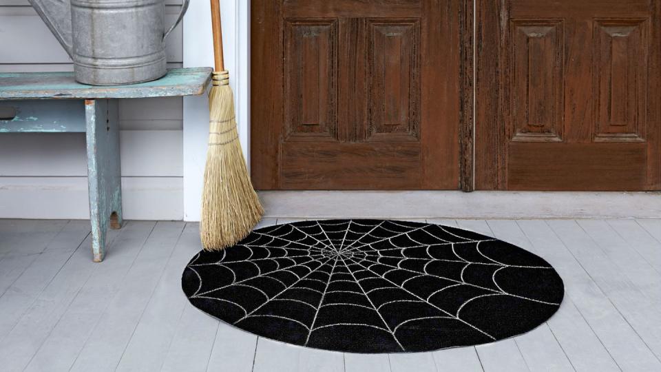 <p>Lure visitors with a spooky doormat.</p><p><strong>Step 1:</strong> Purchase an indoor/outdoor needle-punch carpet. To turn it into a circle: Mark the rug's center point with a white-colored pencil<em>.</em> Measure and mark the distance from that point to a spot about half an inch from the rug's edge. Cut a piece of string to that length. Tie one end of the string to the pencil and secure the other end of the string to the rug's center point with a tack. Pull the string taut and draw a large circle onto the rug; remove the string. Cut out the circle, just inside the white pencil mark, with sharp scissors.</p><p><strong>Step 2:</strong> Using a yardstick, evenly space and draw eight intersecting lines that cross the rug from edge to edge. Between those lines, draw arches around the mat, using our photo as a guide.</p><p><strong>Step 3:</strong> Lastly, coat the rug with a clear finishing spray, like Krylon Make It Last Clear Sealer<em>.</em> to protect your web from trick-or-treating feet. </p>