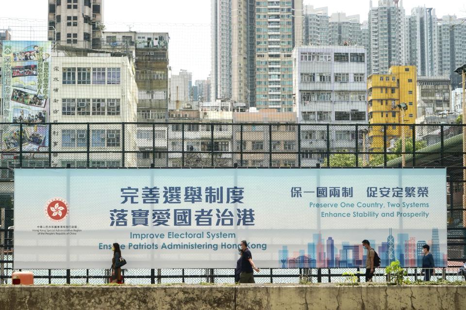 People walk past a government advertisement to promote the new Hong Kong electoral system reform, in Hong Kong, March 30, 2021. China's top legislature approved amendments to Hong Kong's constitution on Tuesday that will give Beijing more control over the make-up of the city's legislature. (AP Photo/Kin Cheung)