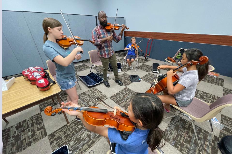 Sinfonia Gulf Coast Youth Orchestra Conductor Aaron King Vaughn and violinist Emily Kent (standing) demonstrate the proper way to hold a violin and use a bow to music students (front to back) Nora Reyes, Amelia Reyes and Tripp Cox during a week-long camp for stringed instruments.