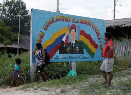 A family stand next to an artwork depicting Venezuela's former President Hugo Chavez in Ivirgarzama in the Chapare region, Bolivia, December 18, 2016. The banner reads, "Banner reads "Education school Hugo Chavez Frias". REUTERS/David Mercado