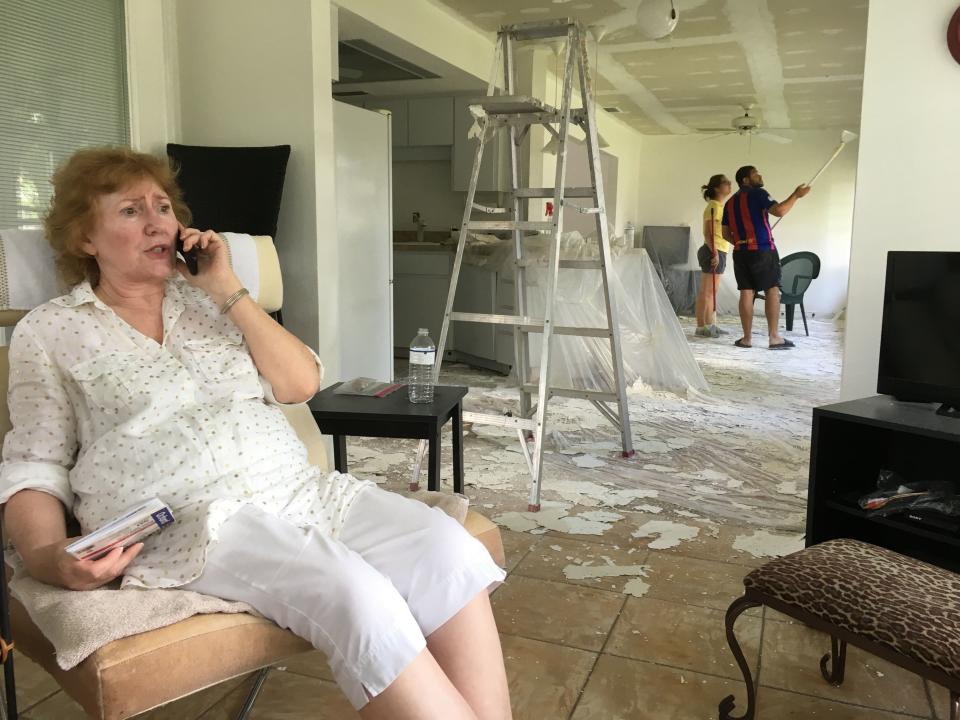 Anita Dennis speaks to her homeowner's insurance company from her south Fort Myers home Monday as church members Arturo and Ruth Maita work to peel off the popcorn ceiling in the wake of Hurricane Irma.