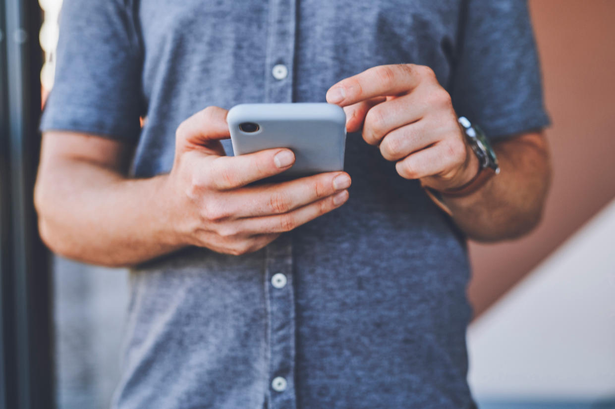 Closeup of a man on a phone browsing on social media while standing outdoors in the city street. Guy reading an article or blog on a website with a smartphone in an urban town road.