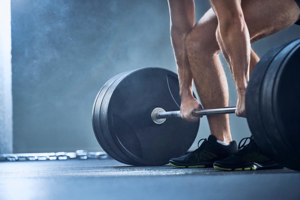 A close up of a man's arms and legs as he prepares to do a heavy deadlift exercise.