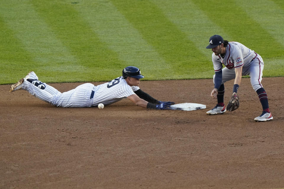 The throw to Atlanta Braves shortstop Dansby Swanson, right, is offline as New York Yankees Gio Urshela, left, slides safely into second on a third-inning double during an interleague baseball game, Tuesday, April 20, 2021, at Yankee Stadium in New York. (AP Photo/Kathy Willens)