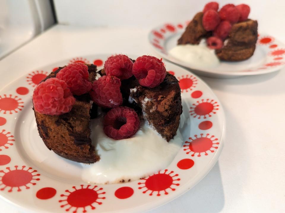 two plates with oozing molten lava cakes topped with raspberries and vanilla cream