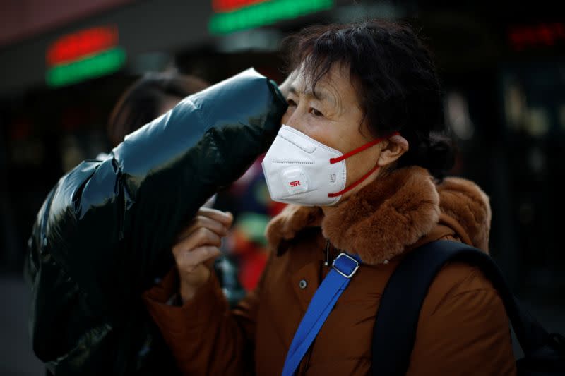 A woman gets help to fit her face mask outside Beijing Railway Station as the country is hit by an outbreak of the new coronavirus, in Beijing