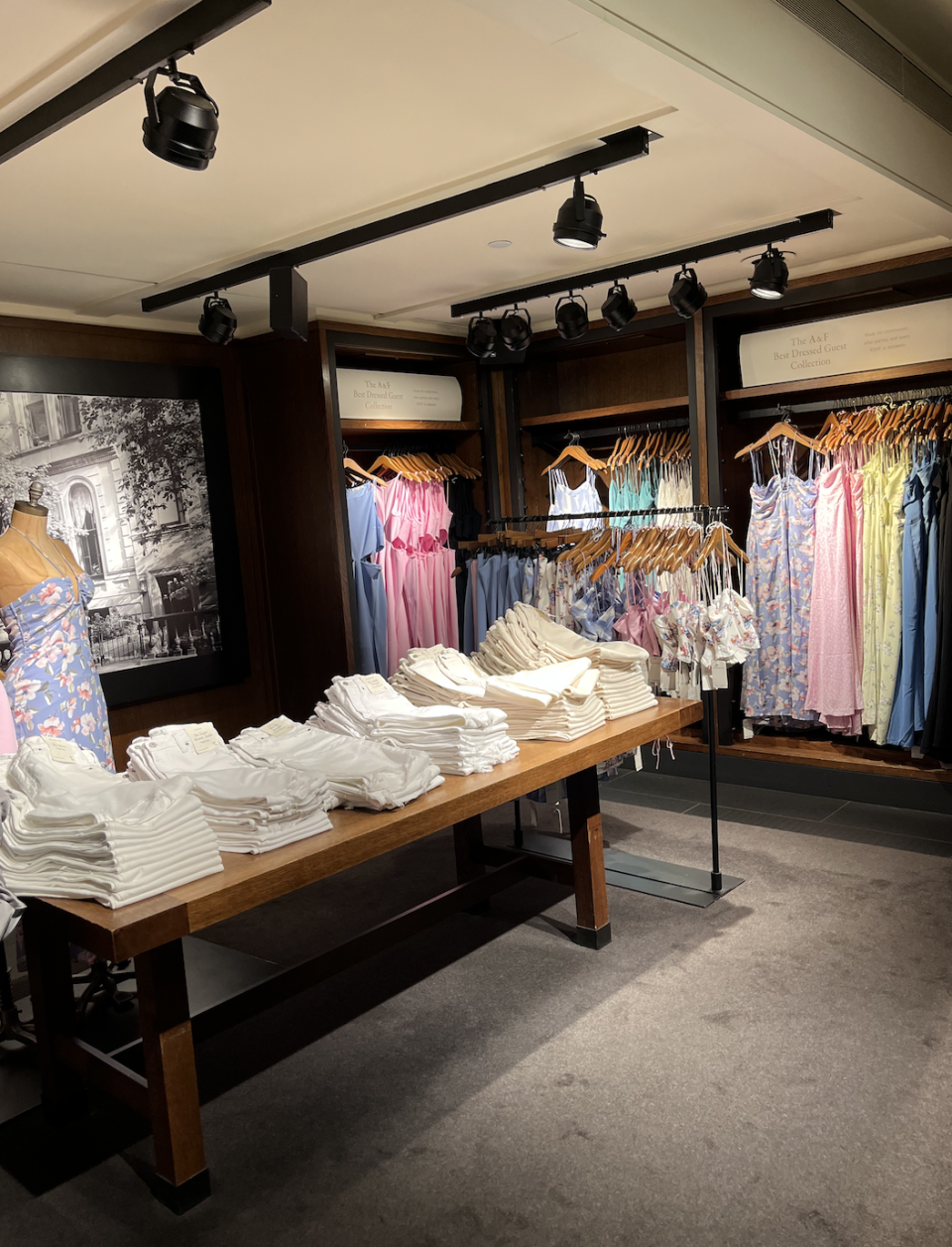 Long, thin-strapped dresses hanging up alongside folded pants on a table and sleeveless tops hanging up