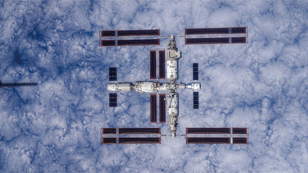  A large T-shaped space station is seen from above with Earth below it. 